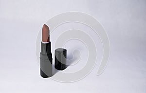 Carrot-colored lipstick stands vertically open with a black cap near in the center on a white background photo