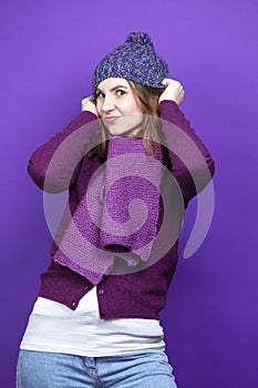 One Caucasian Adult Female Woman In Warm Knitted Hat and Violet Scarf with Lifted Hands Pulling Hat Down While looking Straight On