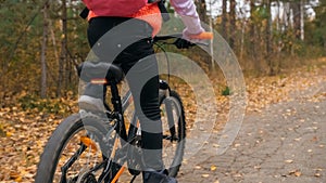 One caucasian children rides bike road in autumn park. Little girl riding black orange cycle in forest. Kid goes do