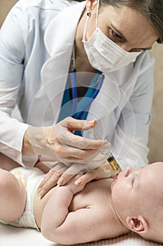 One caucasian female doctor is giving some dose of liquid medicine to infant baby boy by syringe into the mouth from disease or fo