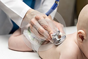 One caucasian female doctor is listening heartbeat of infant boy by stethoscope