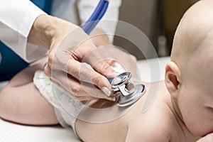 One caucasian female doctor is listening heartbeat of infant boy by stethoscope