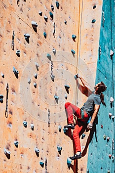 One Caucasian man professional rock climber workouts on climbing wall at training center in sunny day, outdoors. Concept