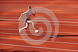 One Caucasian woman, female athlete, runner training at public stadium, sport court or palyground outdoors. Summer sport