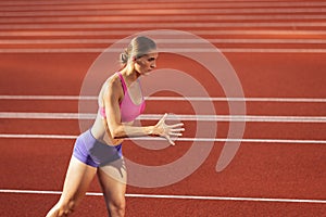 One Caucasian woman, female athlete, runner training at public stadium, sport court or palyground outdoors. Summer sport