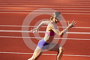 One Caucasian woman, female athlete, runner training at public stadium, sport court or palyground outdoors. Summer sport