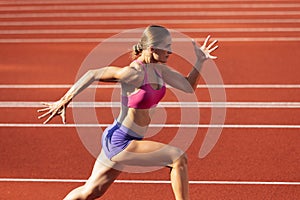 One Caucasian woman, female athlete, runner training at public stadium, sport court or palyground outdoors. Summer sport