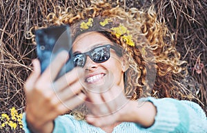 One cheerful beautiful woman taking selfie picture laying down on the ground in forest woods and wearing yellow flowers. People