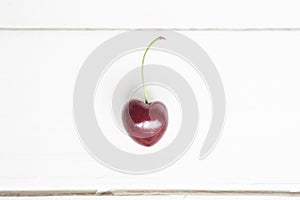 One cherry in the shape of a heart. Ripe fresh juicy berry on a white wooden background. Fruit background. valentine