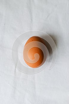 One chicken egg on a white tablecloth. Rustic style. The concept of organic food. Minimalism. Vertical orientation.