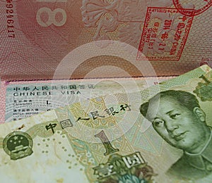 One Chinese yuan is on a passport with a Chinese visa and border stamps.