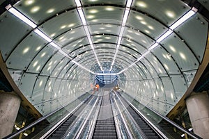 One cleaning staff person in orange coat on escalator at modern, futuristic architecture subway station, arched ceiling