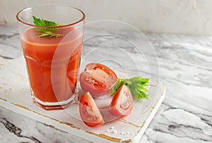 One clear glass cup with red tomato juice and celery leaf, sliced tomato on a white cutting board. Healthy food concept