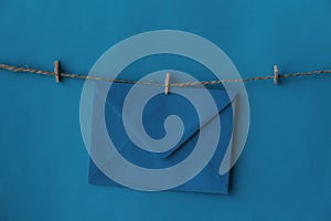 One closed blue envelope hanging on rope isolated blue background.