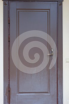 one closed brown metal-plastic door on a gray wall of a house
