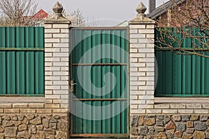 One closed green metal door on a white brick and iron fence