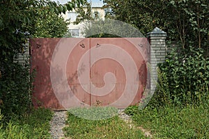 One closed red metal gate and a white wall of a brick fence