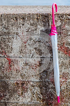 One closed umbrella next to concrete wall