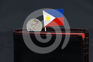 One coin of Philippine peso money and mini Philippine flag stick on the black wallet with dark background