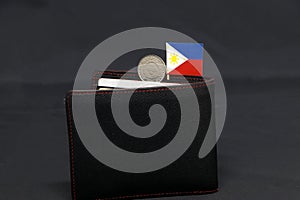 One coin of Philippine peso money and mini Philippine flag stick on the black wallet with dark background