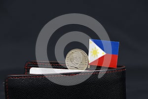 One coin of Philippine peso money and mini Philippine flag stick on the black wallet with dark background