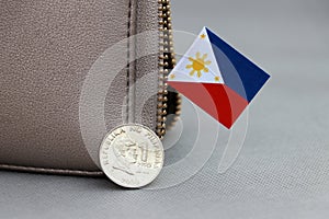 One coin of Philippine peso money on obverse and mini Philippine flag stick on the leather wallet on grey background