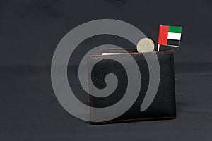 One coin of United Arab Emirates one dirham money and mini UAE flag stick on the black wallet with dark background