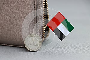 One coin of United Arab Emirates one dirham money on obverse and mini UAE flag stick on the leather wallet on grey background