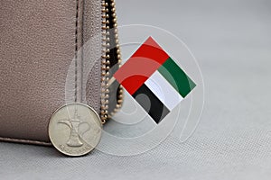 One coin of United Arab Emirates one dirham money on reverse and mini UAE flag stick on the leather wallet on grey background