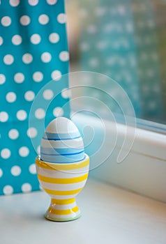 One colorful striped blue Easter egg in vibrant modern egg stand with spotted blue background near window