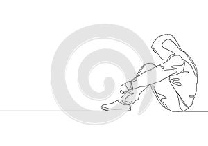 One continuous line drawing of young despair male teen sitting down on the floor wearing hoodie in the city street