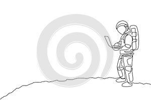 One continuous line drawing of young spaceman on spacesuit standing while typing in moon surface. Astronaut business office with