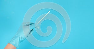 One Cotton stick for swab test in hand with blue medical gloves or latex glove on blue background.covid-19 concept