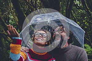 One couple have fun and enjoy bad weather rain under a transparent umbrella smiling together and checking drops water. Outdoor