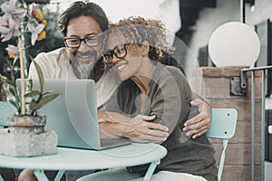 One couple middle age enjoy and have fun together using laptop sitting outdoor at the table in the garden at home. Man and woman