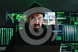 One criminal hacker man programming a phishing virus, at background a lot of data screens. One caucasian developer