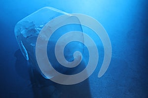 One crystal clear ice cube on light blue background, closeup and space for text. Color tone effect