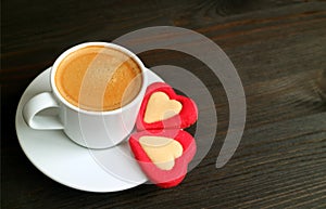 One cup of hot coffee with two heart shaped cookies on dark brown wooden table