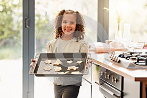 One cute little mixed race girl looking happy and proud while baking alone at home. Hispanic child with curly hair