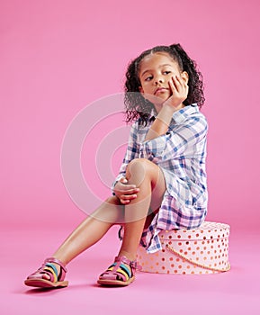 One cute little mixed race girl sitting in a studio and daydreaming against a pink copyspace background. A lonely