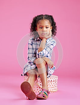 One cute little mixed race girl sitting in a studio and daydreaming against a pink copyspace background. A lonely