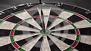 One dart hits the bull's eye of a dartboard on a black wooden background. Happy win and luck concept. Close-up