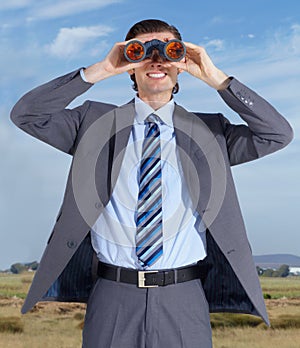 One day Ill conquer the world. A young businessman holding binoculars while standing against a blue sky.