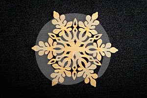 One delicate light brown wooden snowflake on black textile material background, displayed on centre, top view with space for text