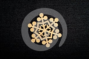 One delicate light brown wooden snowflake on black textile material background, displayed on centre, top view with space for text