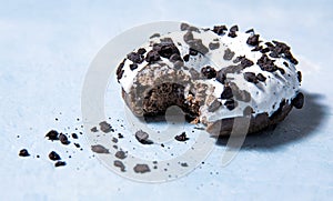 One delicious fresh hearty black and white bitten donut lie on a blue background. jank food and high-calorie food