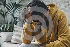 One desperate frustrated man alone at home holding his head on hand looking down. Stress and bad mental health condition concept.