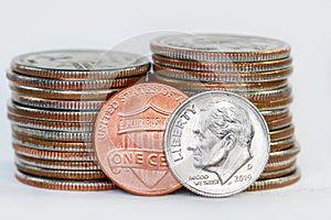 One dime and cent against stack of American quarter coins.