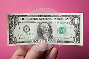 One dollar in hand on a pink background