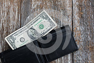 One dollar is lying in an empty leather wallet. No money in the purse. Poverty and unemployment. Old wooden rustic background